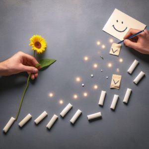 Pratiquer la gratitude avec la fibromyalgie. Une série d'actions simples (comme donner une fleur, sourire, écrire une note) qui créent une traînée de lumière positive, symbolisant l'effet domino des actes de gratitude.
